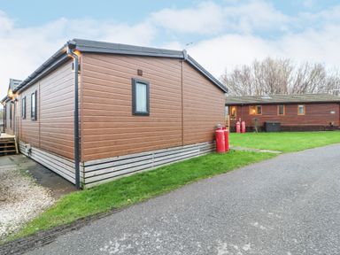 An outdoor area with two brown wooden lodges and red gas cylinders on grass at 12A Lake Escape in Carnforth