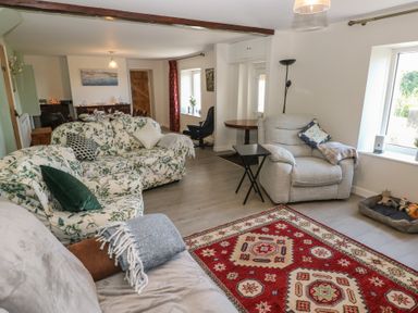 A living room with floral sofas a grey armchair a red patterned rug and a dining area at Chapel Hill House in Chapel Hill near Pembroke