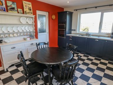 A kitchen with black and white checkered floor a black round table with four chairs dark blue cabinets a white plate rack and an orange wall at Chapel Hill House Chapel Hill near Pembroke