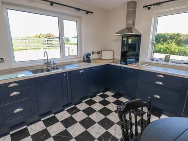 A kitchen with blue cabinets black and white checkered floor and two large windows at Chapel Hill House in Chapel Hill near Pembroke