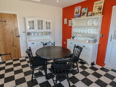 A dining area with a black round table and four black chairs white cabinets with dishes and cups against white and red walls at Chapel Hill House Chapel Hill near Pembroke