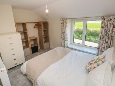 A bedroom with a bed near a window with floral curtains and open shelving units at Chapel Hill House in Chapel Hill near Pembroke