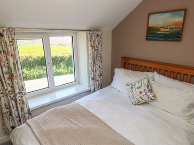 A bedroom with a wooden bed white bedding floral pillow and curtains and a painting of a boat on the wall at Chapel Hill House in Chapel Hill near Pembroke