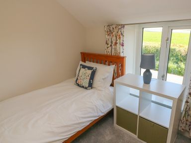 A small bedroom with a single bed a floral cushion a white storage unit with a lamp and floral curtains at Chapel Hill House Chapel Hill near Pembroke