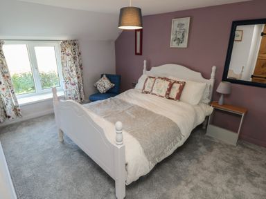 A bedroom with a white bed and a floral pillow near a window with floral curtains at Chapel Hill House in Chapel Hill near Pembroke