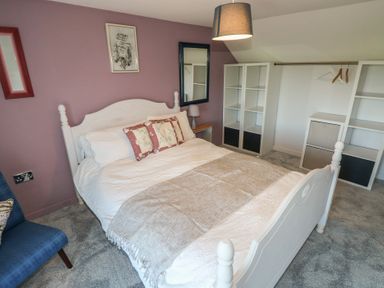 A bedroom with a white bed and floral pillows a purple wall with mirrors and shelves at Chapel Hill House Chapel Hill near Pembroke