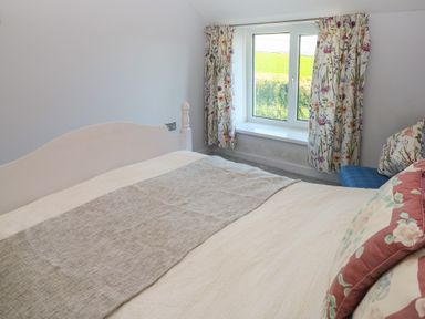 A bedroom with a white bed and floral curtains by a window at Chapel Hill House in Chapel Hill near Pembroke