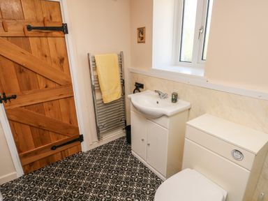 A bathroom with a wooden door a white sink and cabinet a white toilet a towel rack with a yellow towel and a small window at Chapel Hill House Chapel Hill near Pembroke