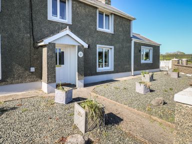 The front exterior of a grey house with white trim and a white door with a small porch surrounded by gravel and rectangular planters at Chapel Hill House in Chapel Hill near Pembroke