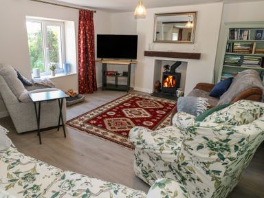 A living room with floral armchairs a gray sofa a red patterned rug a wood-burning stove and a bookshelf at Chapel Hill House Chapel Hill near Pembroke