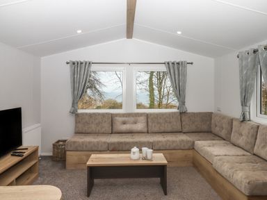 A living room with an L shaped sofa a wooden coffee table a television and windows with curtains at 5 Manor Park in Bucks Cross Bideford