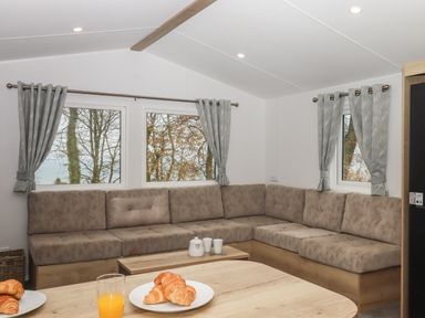 A living room with an L shaped sofa and gray curtains on windows at 5 Manor Park in Bucks Cross Bideford
