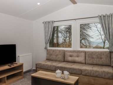 A living room with a sofa a wooden coffee table with a teapot and cups a television and windows with curtains at 5 Manor Park in Bucks Cross Bideford
