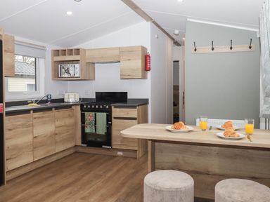 A kitchen with wooden cabinets a stove microwave toaster and a dining table with croissants and orange juice at 5 Manor Park in Bucks Cross Bideford