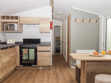 A kitchen area with wooden cabinets a black stove a microwave toaster and a dining table with plates of croissants at 5 Manor Park in Bucks Cross Bideford