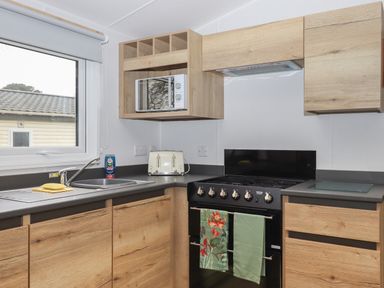 A kitchen with wooden cabinets a black stove a microwave a toaster and a sink at 5 Manor Park in Bucks Cross Bideford