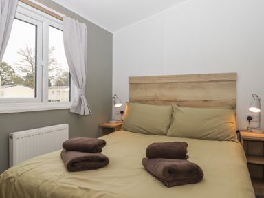 A bedroom with a double bed with folded towels on it next to a window with light curtains at 5 Manor Park in Bucks Cross Bideford