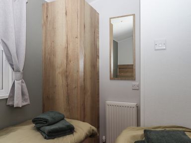 A bedroom corner with two beds folded towels on each bed a wooden wardrobe a wall mirror radiator and a light switch at 5 Manor Park Bucks Cross Bideford