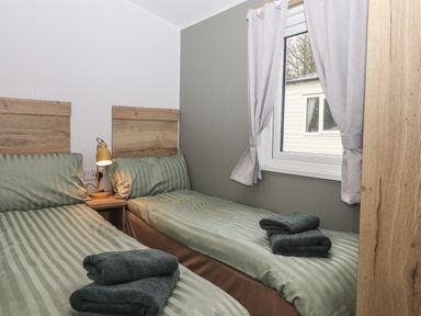 A bedroom with two single beds with green striped bedding and folded towels by a window with curtains at 5 Manor Park in Bucks Cross Bideford