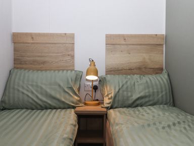 Two single beds with wooden headboards and green striped bedding with a wooden nightstand and yellow lamp between them at 5 Manor Park in Bucks Cross Bideford