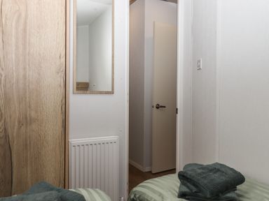 A bedroom corner with a wooden wardrobe a mirror a radiator an open door and folded towels on a bed at 5 Manor Park Bucks Cross Bideford