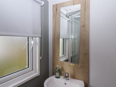A bathroom sink with soap dispenser a wooden framed mirror and a window with a roller blind at 5 Manor Park in Bucks Cross Bideford