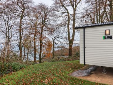 An outdoor scene showing trees with autumn leaves and part of a white mobile home on grass at 5 Manor Park in Bucks Cross Bideford