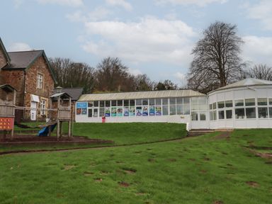 A playground with wooden climbing structures next to a building with glass windows and a sign for swimming pools at 5 Manor Park in Bucks Cross Bideford