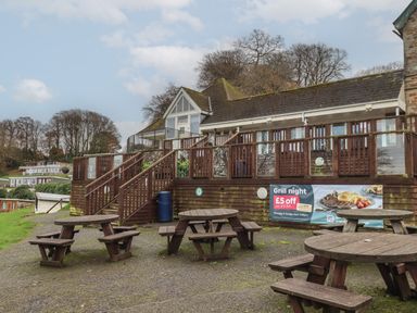 Outdoor seating area with wooden picnic tables and a building with a deck and stairs at 5 Manor Park in Bucks Cross Bideford