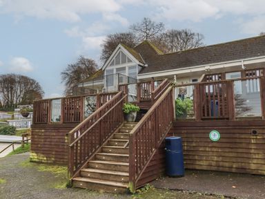 An outdoor wooden staircase leading to a building with glass doors and windows surrounded by trees at 5 Manor Park in Bucks Cross Bideford