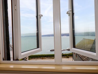 A view through an open window overlooking the sea with a distant coastline and buildings at Blue Horizon in Port Isaac