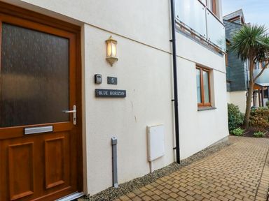 The exterior entrance of a unit with a wooden door window and signs for number 5 and Blue Horizon an outdoor path and foliage at Blue Horizon Port Isaac