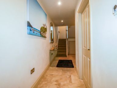 A hallway with stairs at the end a glass table a mirror and a painting on the wall at Blue Horizon in Port Isaac