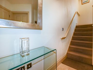 A staircase with carpeted steps and a railing next to a wall with a large mirror and a glass table holding a glass vase at Blue Horizon in Port Isaac