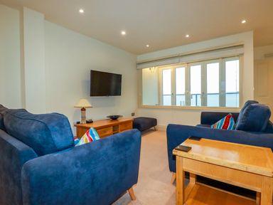 A living room with blue sofas wooden tables a wall-mounted television and large windows at Blue Horizon in Port Isaac