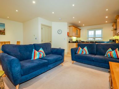 A living room with two blue sofas and striped pillows and a kitchen area in the background at Blue Horizon in Port Isaac