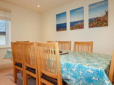 A dining room with a wooden table and chairs a floral tablecloth and three ocean and flower paintings on the wall at Blue Horizon in Port Isaac