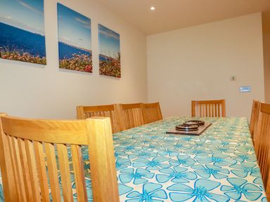 A dining room with wooden chairs and a table covered with a blue floral tablecloth and three landscape pictures on the wall at Blue Horizon in Port Isaac