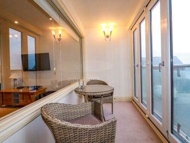 A small indoor seating area with two wicker chairs and a round wicker table near glass doors with a view at Blue Horizon in Port Isaac