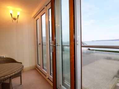 A room with wicker furniture next to large glass doors opening to a balcony with an ocean view at Blue Horizon in Port Isaac