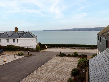 A view of the sea with a paved parking area and buildings with slate roofs in the foreground at Blue Horizon in Port Isaac