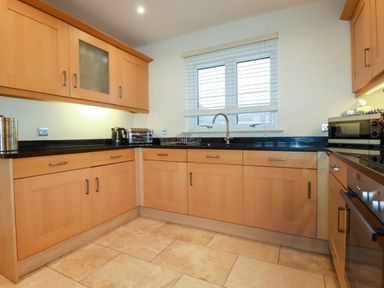 A kitchen with wooden cabinets black countertops window above the sink and various appliances at Blue Horizon in Port Isaac