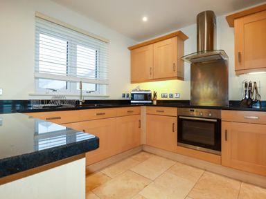 A kitchen with wooden cabinets black countertops a stainless steel oven range hood microwave and a window with blinds at Blue Horizon in Port Isaac