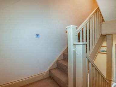 A carpeted staircase with white wooden banisters and a wall with a power outlet at Blue Horizon in Port Isaac