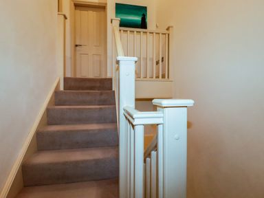 A staircase with beige carpet and white wooden banister leading to a closed door at Blue Horizon in Port Isaac