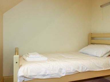 A single bed with white sheets, a pillow, and folded towels on top in a small room at Blue Horizon in Port Isaac