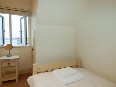 A bedroom with a bed towels on it a bedside table with a mirror and an open window at Blue Horizon in Port Isaac