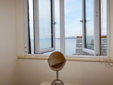 A room with an open window overlooking the sea and a round mirror on a table at Blue Horizon in Port Isaac