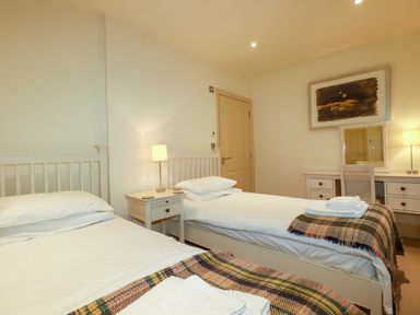 A bedroom with two single beds a nightstand with a lamp a dresser with a mirror and chair at Blue Horizon in Port Isaac