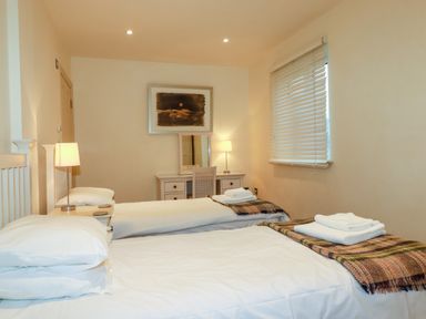 A bedroom with two single beds a desk with a chair and two table lamps at Blue Horizon in Port Isaac